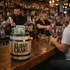 Custom engraved oak barrel tip jar on a bar as a customer adds cash while a bartender gives a thumbs up, showcasing bar promotion and branding
