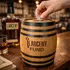 Engraved Larceny Fund oak barrel piggy bank with coin slot on a distillery bar as a hand drops a coin in, showcasing branded distillery gift shop merchandise